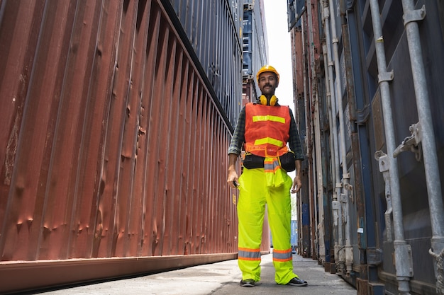 Engenheiro barbudo em pé com capacete amarelo para controlar o carregamento e verificar a qualidade dos contêineres