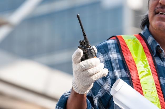 Engenheiro civil asiático sênior não identificado, usando luvas, segurando o walkie-talkie