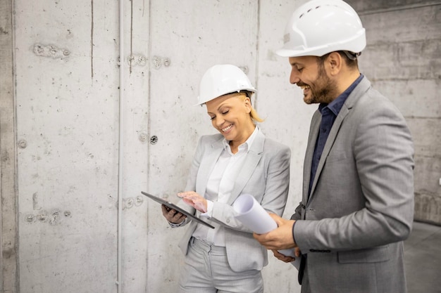 Engenheiro civil e designer de interiores visitando o canteiro de obras e discutindo sobre o plano do projeto