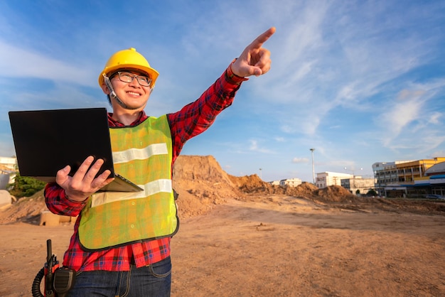 Engenheiro civil técnico asiático usa tablet com tecnologia de caneta inteligente na construção do local de transporte para inspecionar o trabalho de engenharia de planta on-line com a equipe na hora do pôr do sol