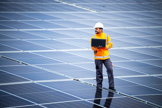 Engenheiro com laptop caminhando por uma grande usina de energia solar