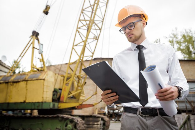 Foto engenheiro construtor em um capacete segura desenhos no local de construção