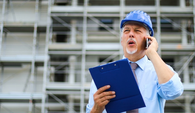 Engenheiro construtor no canteiro de obras falando ao telefone