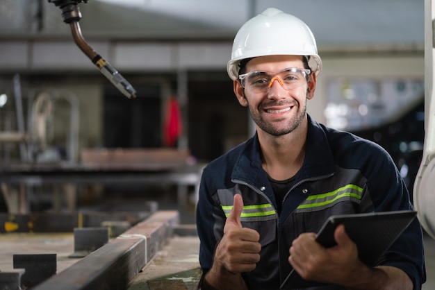 engenheiro de automação masculino sorrindo segurar tablet para máquina de solda de braço de robô de inspeção na fábrica