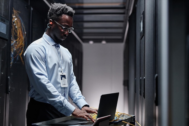 Engenheiro de dados retroiluminado usando laptop na sala do servidor