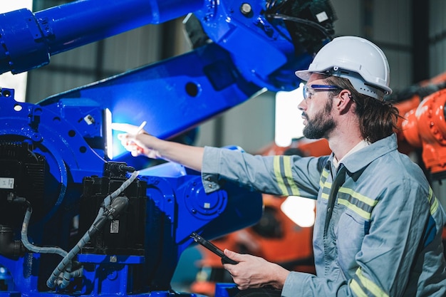 Foto engenheiro de fábrica inspecionando a máquina com tablet inteligente o trabalhador trabalha no braço do robô da máquina pesada a máquina de solda com um sistema remoto em uma fábrica industrial conceito de inteligência artificial