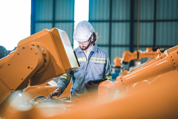 Engenheiro de fábrica inspecionando a máquina com tablet inteligente O trabalhador trabalha no braço do robô da máquina pesada A máquina de solda com um sistema remoto em uma fábrica industrial Conceito de inteligência artificial