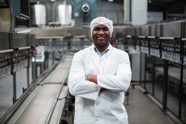 Engenheiro de fábrica sorridente em pé com os braços cruzados na fábrica de garrafas