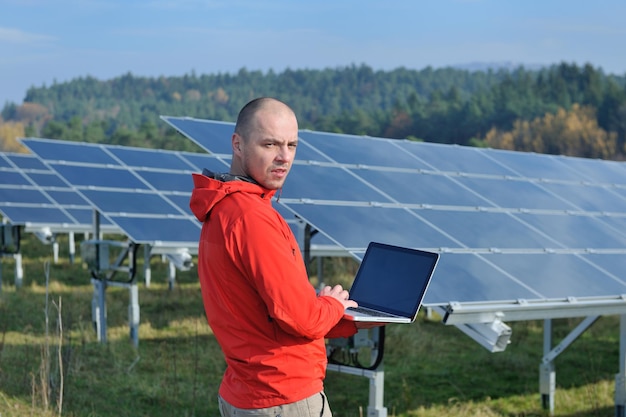 engenheiro de homem de negócios usando laptop em painéis solares planta campo de energia ecológica em segundo plano