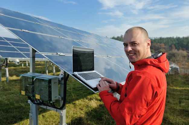 engenheiro de homem de negócios usando laptop em painéis solares planta campo de energia ecológica em segundo plano