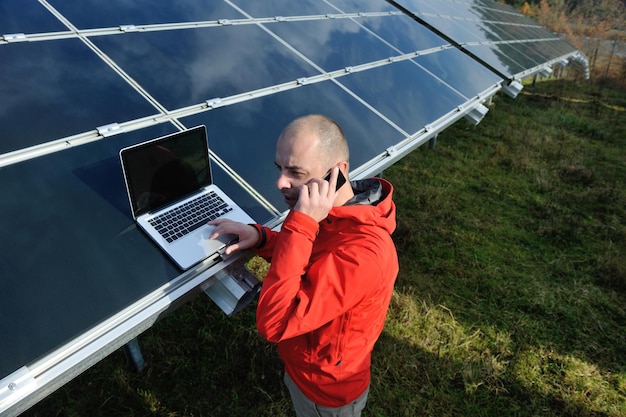 engenheiro de homem de negócios usando laptop em painéis solares planta campo de energia ecológica em segundo plano