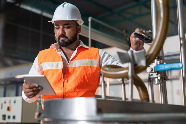 Foto engenheiro de homem segura tablet e repara máquina de pressão de caldeira de tubo em fábrica de alimentos e bebidas