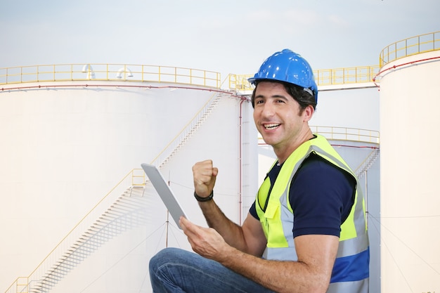 Engenheiro de inspeção segurando computador tablet contra tanques de combustível no local da indústria.