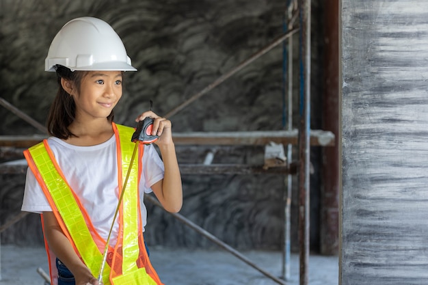 Engenheiro de menina usa camisa de segurança e capacete de segurança segurando a fita métrica no canteiro de obras. Aprendizagem e conceito de trabalho dos sonhos.