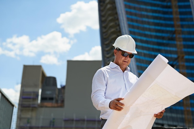 Engenheiro de planos ou homem que lê na cidade no local de construção para desenvolvimento ou manutenção de renovação Arquiteto de plano de piso ou pessoa com documento de projeto ou papel para projeto de construção ao ar livre