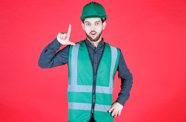 Engenheiro de uniforme verde e capacete mostrando sinal de perdedor.