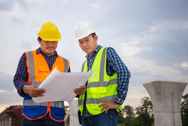 Engenheiro e capataz verificando projeto no canteiro de obras Engenheiro e construtores em capacetes discutindo planta no canteiro de obras Conceitos de trabalho em equipe