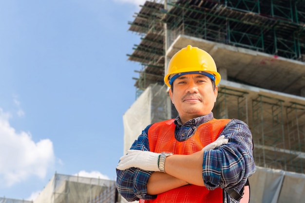 Engenheiro homem / trabalhador com traçado de recorte, verificação e planejamento de projeto no canteiro de obras, sorrindo homem sobre fundo desfocado