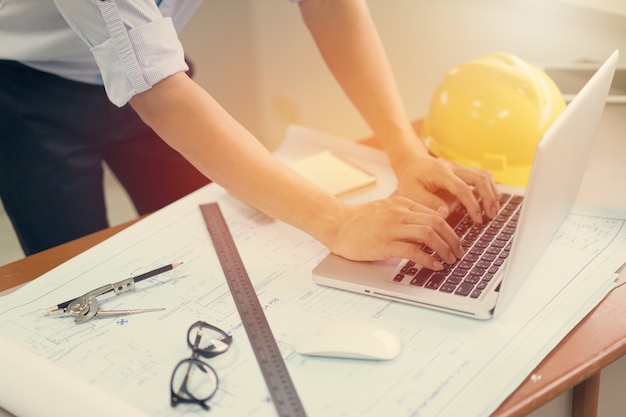 Engenheiro homem trabalhando com laptop e plantas esboçar um projeto de construção