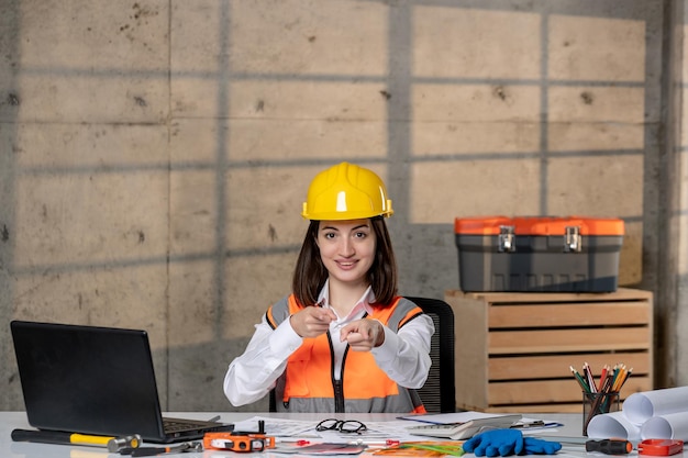 Foto engenheiro inteligente jovem morena trabalhadora civil em capacete e colete apontando para você