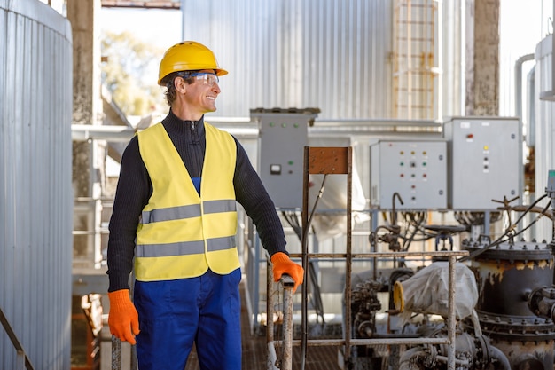 Engenheiro masculino alegre em pé perto de tubos de metal na fábrica