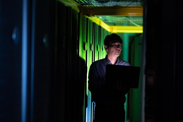 Foto engenheiro masculino asiático usando laptop enquanto inspeciona na sala de servidores de computador. conceito de gerenciamento e manutenção de servidor de banco de dados