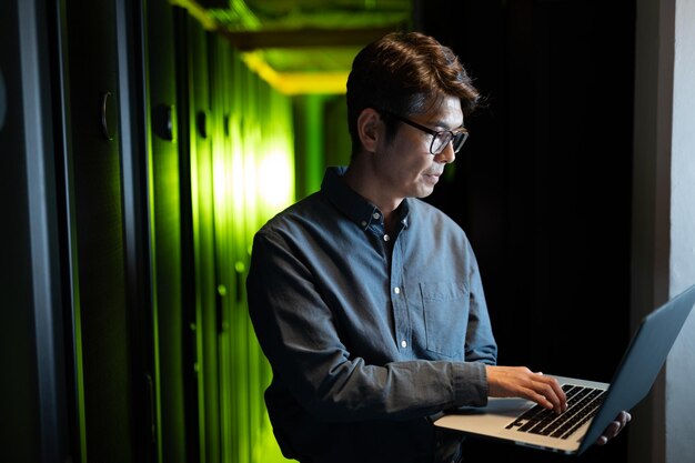 Engenheiro masculino asiático usando laptop na sala de servidores de computador. conceito de gerenciamento e manutenção de servidor de banco de dados
