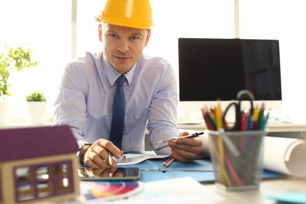 Engenheiro masculino com capacete amarelo sentado no escritório