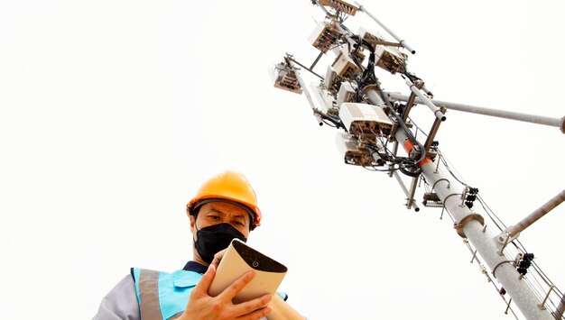 Engenheiro masculino usa tablet de trabalho para se conectar à rede 5G perto da torre de telecomunicações controla o celular