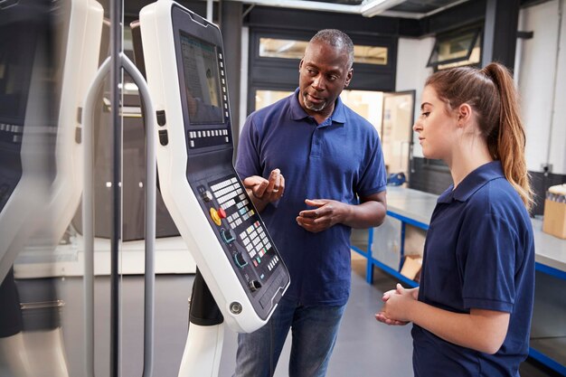 Engenheiro mostrando ao aprendiz como usar a máquina de fabricação de ferramentas CNC