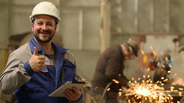 Engenheiro olhando para a câmera sorrindo e mostrando o polegar para cima na planta de metalurgia