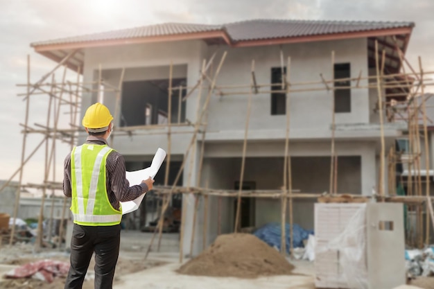 engenheiro profissional em capacete de proteção e papel de plantas no canteiro de obras de construção de casas