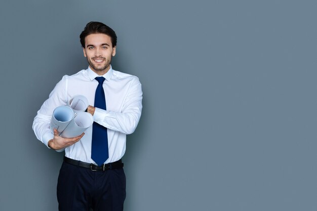 Engenheiro profissional. Homem confiante, simpático e atraente, sorrindo e segurando seus desenhos enquanto trabalhava em um projeto