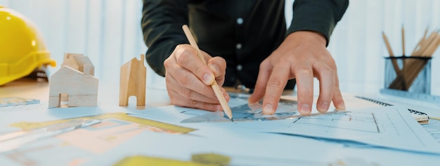 Engenheiro profissional medindo o projeto Engenheiro profissional trabalhando em projeto arquitetônico em estúdio em uma mesa com capacete amarelo e equipamentos arquitetônicos espalhados Delineação