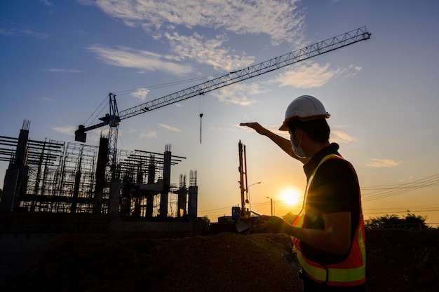 Engenheiro profissional trabalha em um canteiro de obras Plano de trabalho do projeto para projetar casas e edifícios industriais no local de construção ao pôr do sol à noite