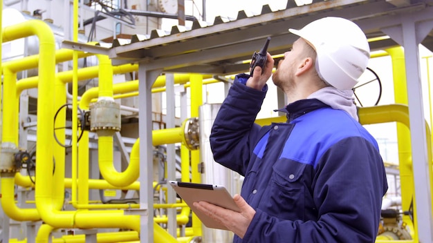 Engenheiro segurando um tablet falando no walkietalkie na fábrica industrial moderna