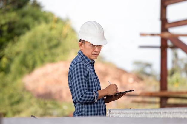 Engenheiro verificando projeto no canteiro de obras Foreman em capacete de segurança com tablet digital no canteiro de obras de infraestrutura