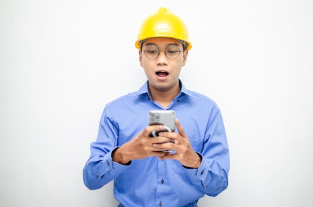 engenheiro vestindo um colete de segurança laranja e um capacete amarelo segurando um telefone com surpresa chocada