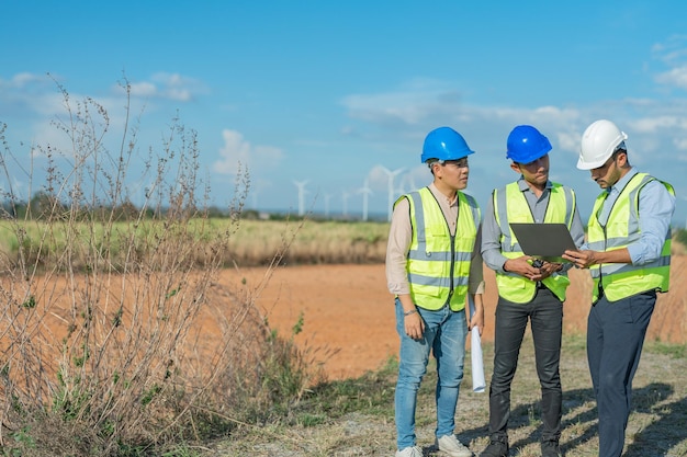 Engenheiros asiáticos trabalhando em trabalho de campo ao ar livre Trabalhadores caminhando e inspecionando a construção e a máquina em torno do local do projeto Turbina eólica elétrica de energia limpa e ambiente sustentável