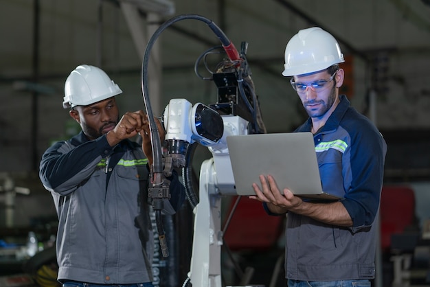 Engenheiros do sexo masculino consertando e inspecionando a máquina de solda do braço do robô com laptop na fábrica