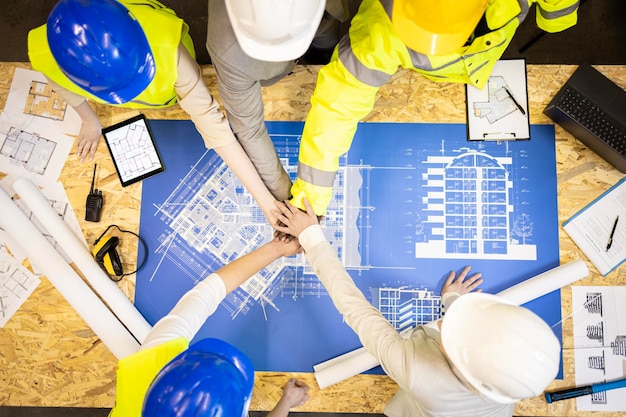 Engenheiros estruturais e arquitetos de mãos dadas acima de planos de construção e plantas