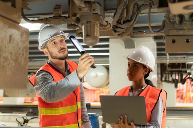 Engenheiros masculinos e femininos trabalham juntos numa estação de reparação elétrica, inspeccionando o chassi.