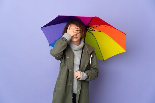 Englische Frau, die einen Regenschirm isoliert hält, der Augen durch Hände bedeckt