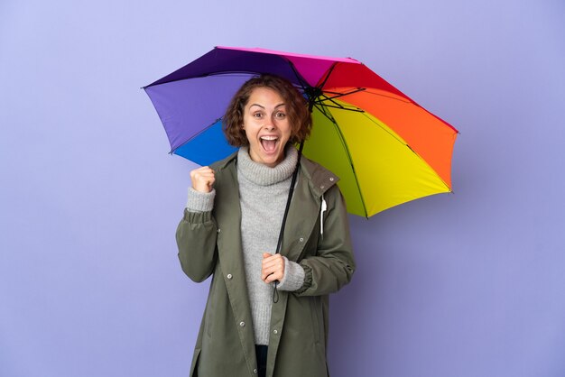 Englische Frau, die einen Regenschirm isoliert hält, der einen Sieg in der Siegerposition feiert