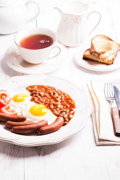 Englisches Frühstück - Eier, Würstchen mit Bohnen und Tee mit Milch