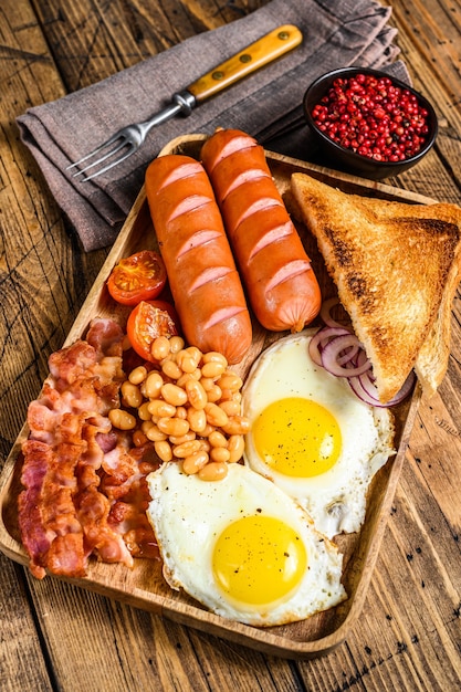 Englisches Frühstück in einem Holztablett mit Spiegeleiern, Würstchen, Speck, Bohnen und Toast.