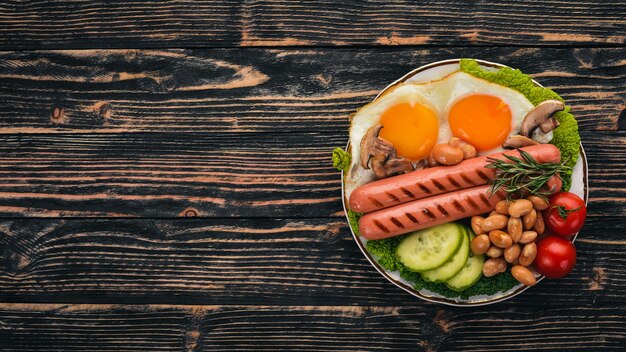 Englisches Frühstück Spiegelei Bohnen Tomaten Pilze Speck und Toast Ansicht von oben auf einem hölzernen Hintergrund