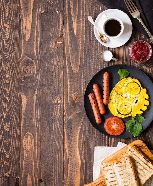 Englisches Frühstück. Spiegeleier, Würstchen, Bohnen, Toastbrot, Tomaten, Käse auf Holz