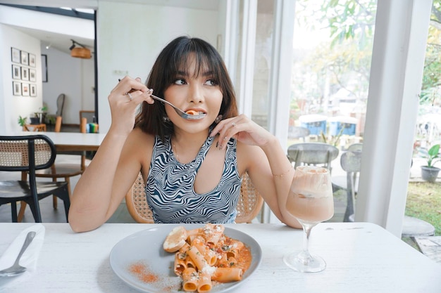 Engraçada jovem asiática comendo macarrão saboroso no café