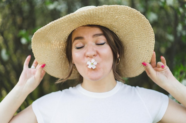 Engraçada jovem mulher bonita com um chapéu entre árvores floridas. Respire livre. Mulher feliz sem alergia